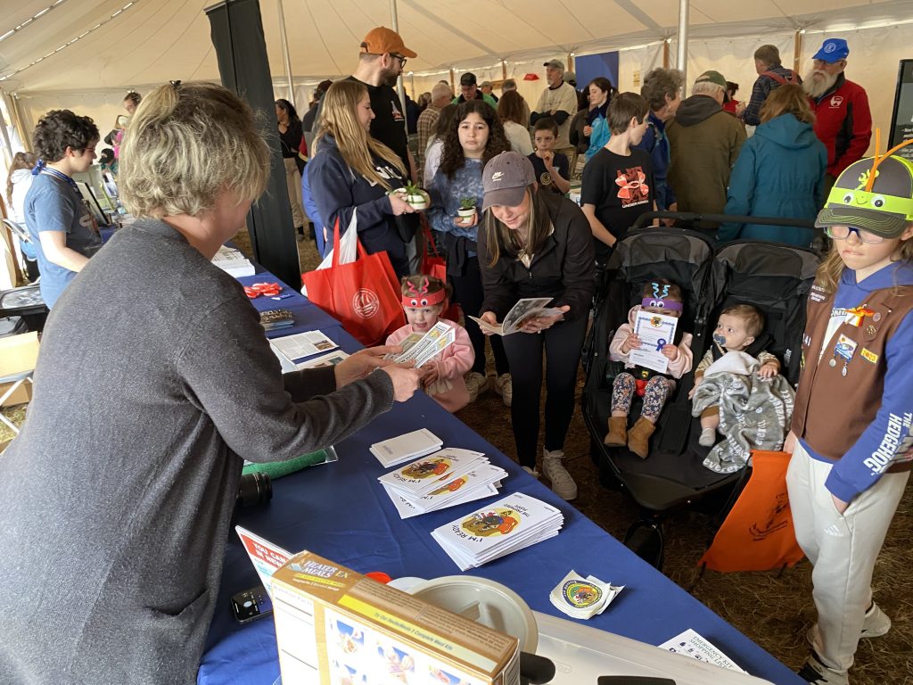 An HSEM employee hands out bookmarks to a gaggle of children in a crowded tent