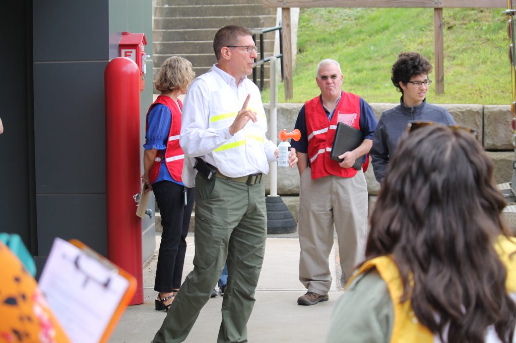 A group of H S E M employees wearing color coded vests listen as a briefing is given outside the emergency room of Concord Hospital's Laconia location.