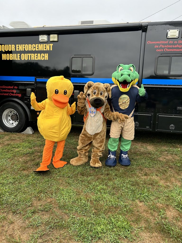 The Choose Love duck, Ready the Prepared Puppy and the Invest-a-gator stand in front of the liquor enforcement vehicle